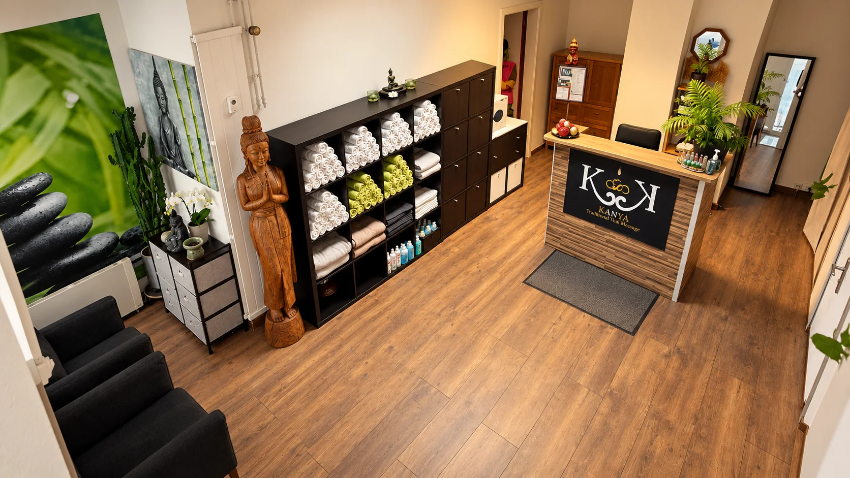 Empfangsbereich von KANYA von oben: Theke mit KANYA-Logo, Handtuchregal, Buddah-Statuen, Wartesofa und Spiegel